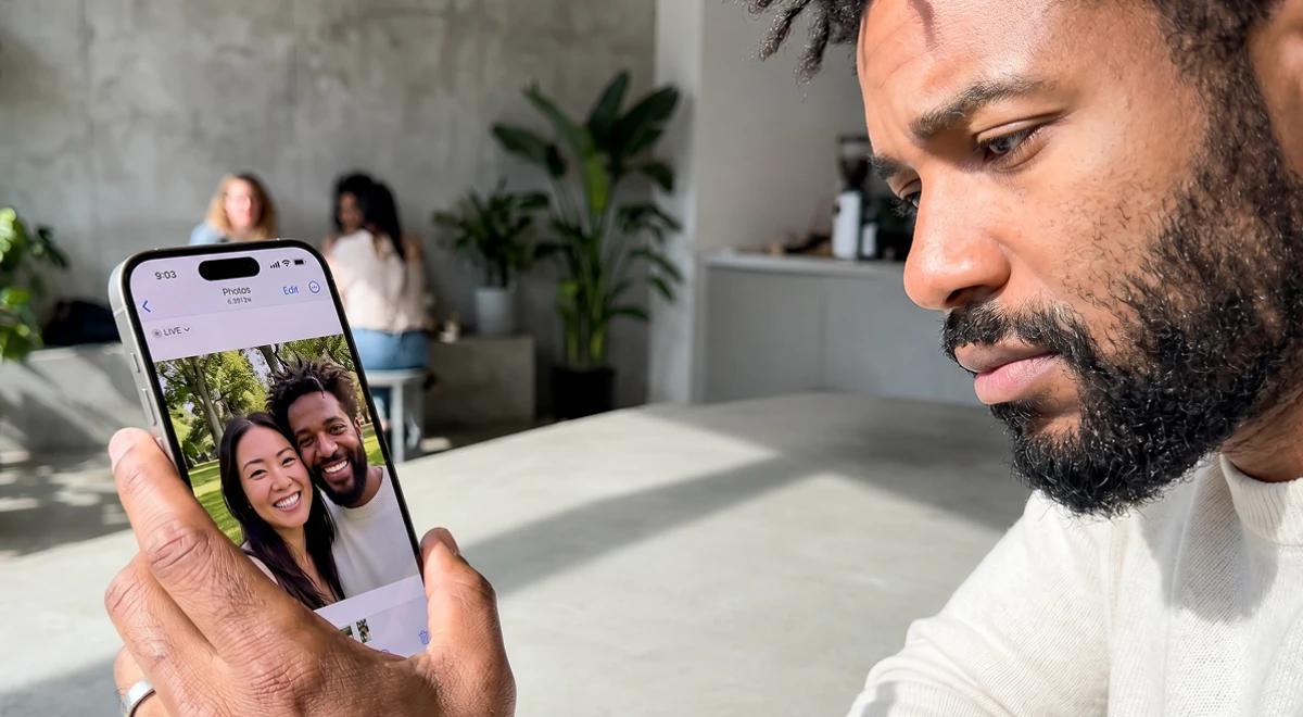 Sad Black man looking at a couples photo on his iPhone in a bright room with plants, representing grief after a break up