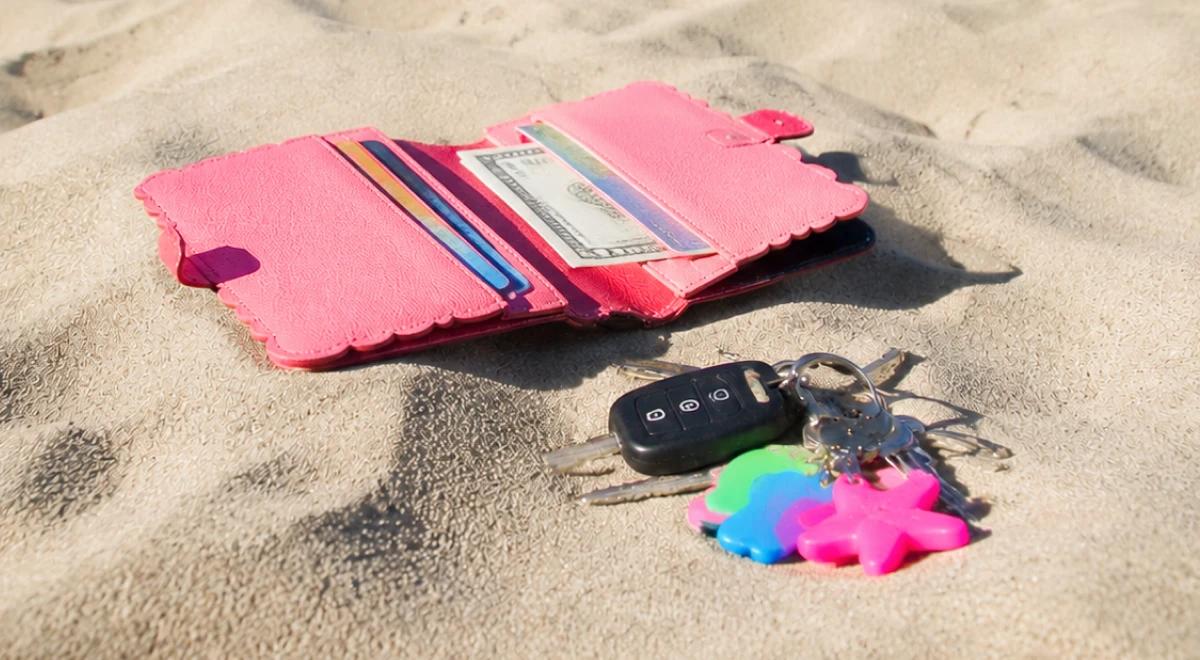 Open pink wallet with cash and cards next to car keys with a colorful keychain left on sandy ground, representing a found belongings moral dilemma