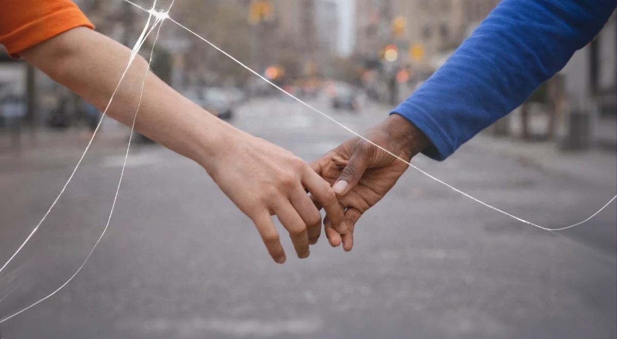 Two people in colorful sleeves barely touching fingertips on a blurred city street, with cracked glass overlay symbolizing a broken relationship
