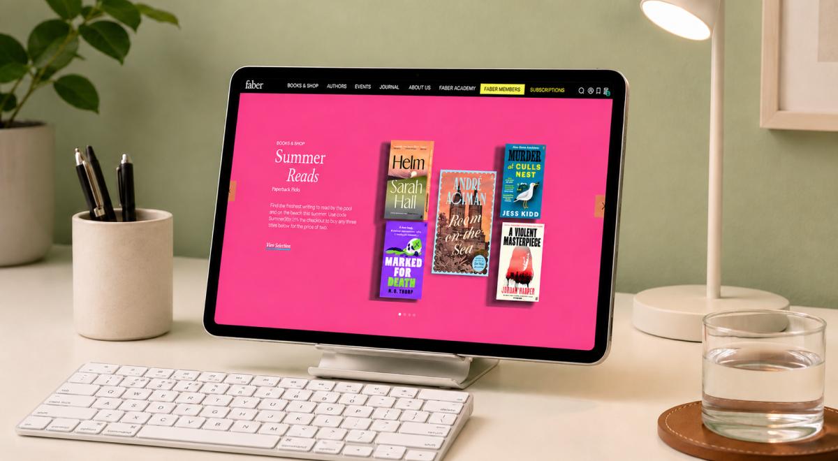 Faber and Faber website Summer Reads page shown on a tablet on a desk with keyboard, pen holder, glass of water and plant against a green wall