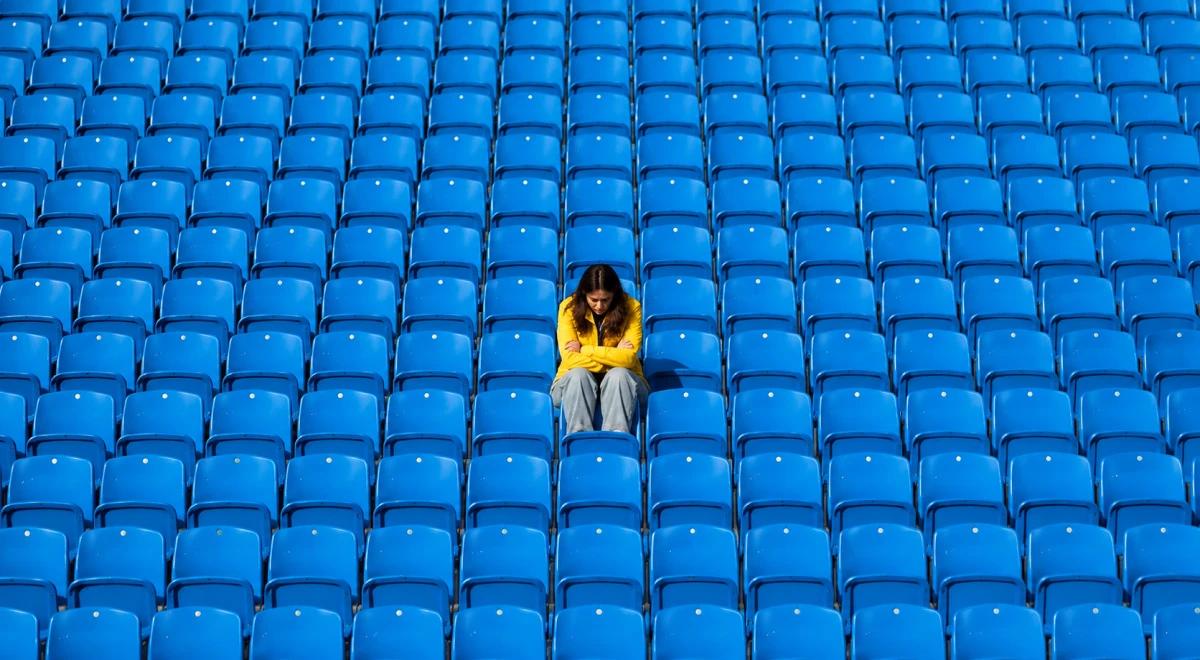 _Lonely person in a yellow hoodie sitting alone among rows of empty blue stadium seats, symbolizing loneliness and emotional isolation after a breakup