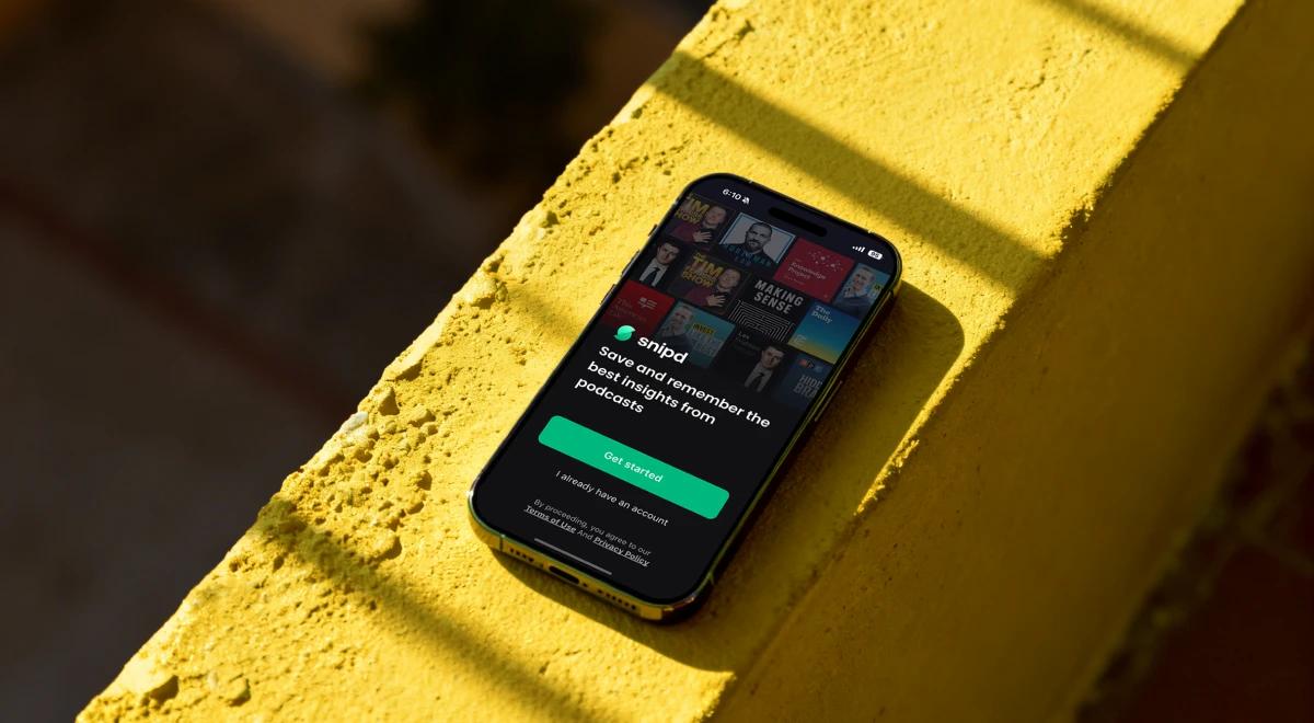 Smartphone displaying the Snipd app welcome screen resting on a yellow textured surface in dramatic lighting, showcasing the podcast insight-saving app