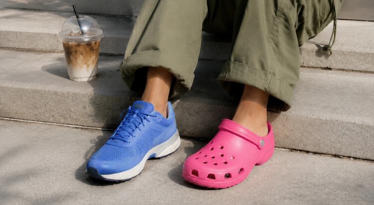Person sitting on steps wearing mismatched footwear — one in blue sneakers, one in pink Crocs — with an iced coffee nearby, illustrating a casual moral dilemma scenario
