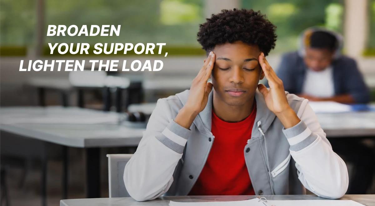 Stressed teenage boy in a varsity jacket holding his temples at a classroom desk with other students in the background, illustrating the need to build secure bonds