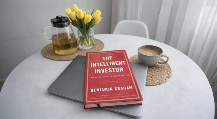 The intelligent investor by benjamin graham on the table with yellow tulips and a teapot