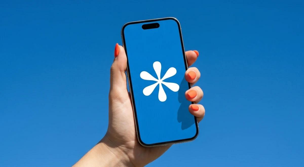 Hand with orange nails holding a smartphone displaying the SparkNotes app logo on a blue background against a bright blue sky