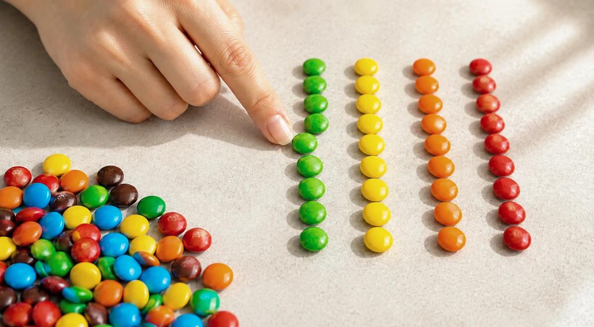 Hand sorting colorful candy pieces into neat rows by color on a beige surface, illustrating OCD-like organizing behavior as a sign of feeling stuck