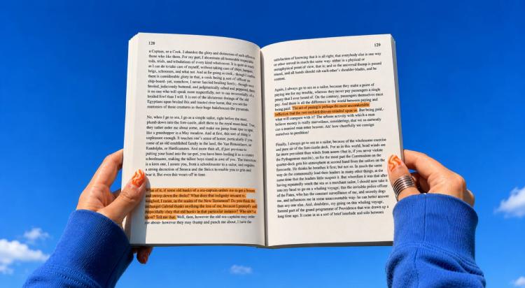 Person in a blue sweater holding open a highlighted paperback book against a bright blue sky with clouds, representing literature reading and book trivia