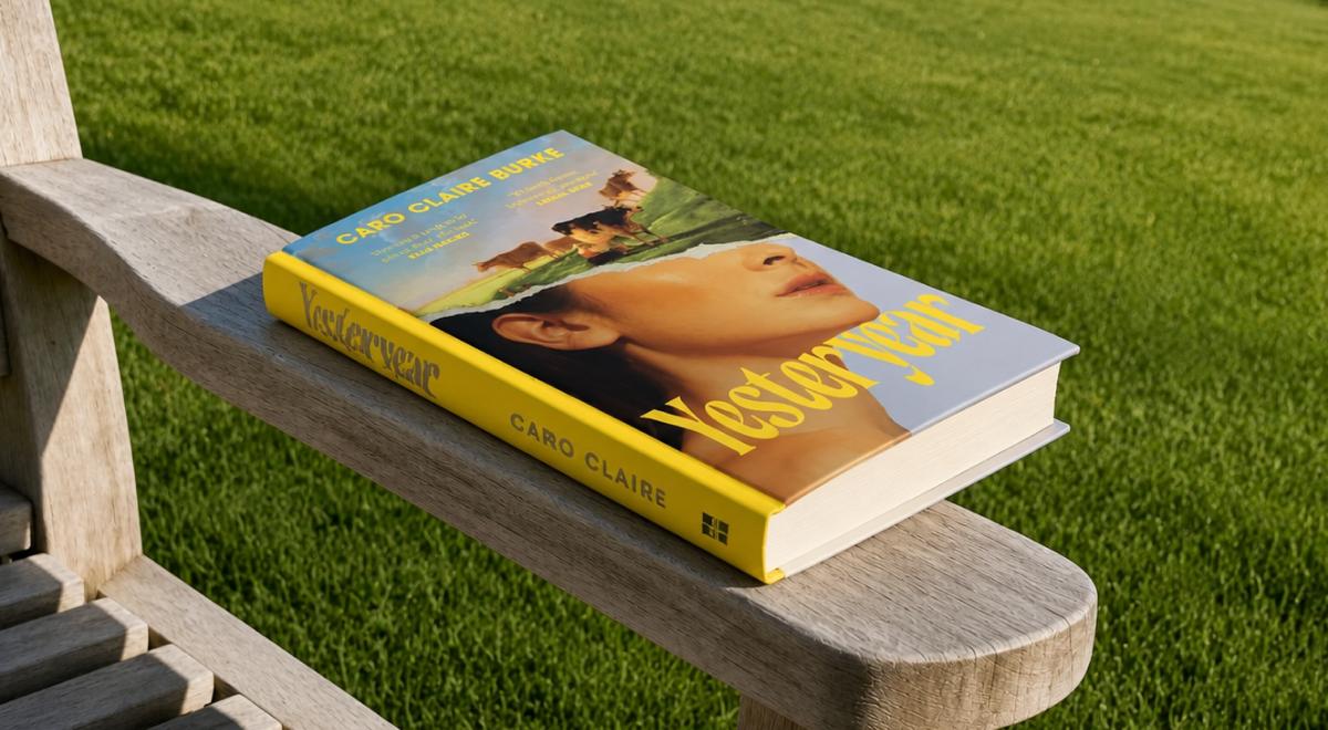Yesteryear book by Caro Claire Burke resting on a weathered wooden garden chair, its yellow cover facing up against a backdrop of sunlit green grass