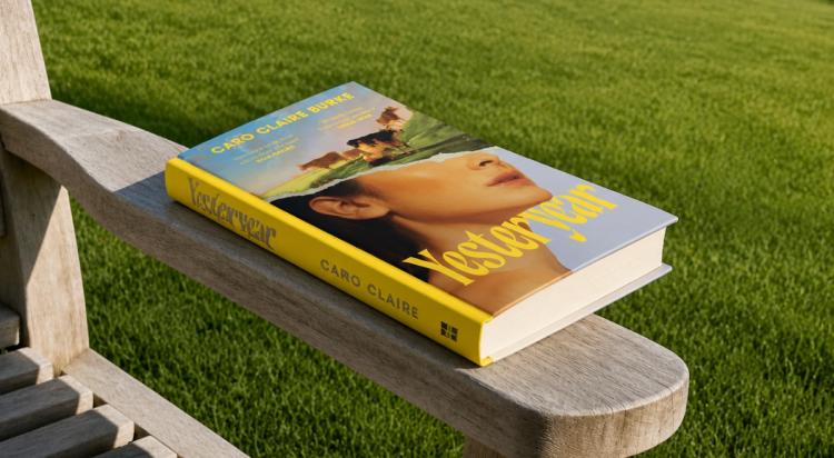 Yesteryear book by Caro Claire Burke resting on a weathered wooden garden chair, its yellow cover facing up against a backdrop of sunlit green grass