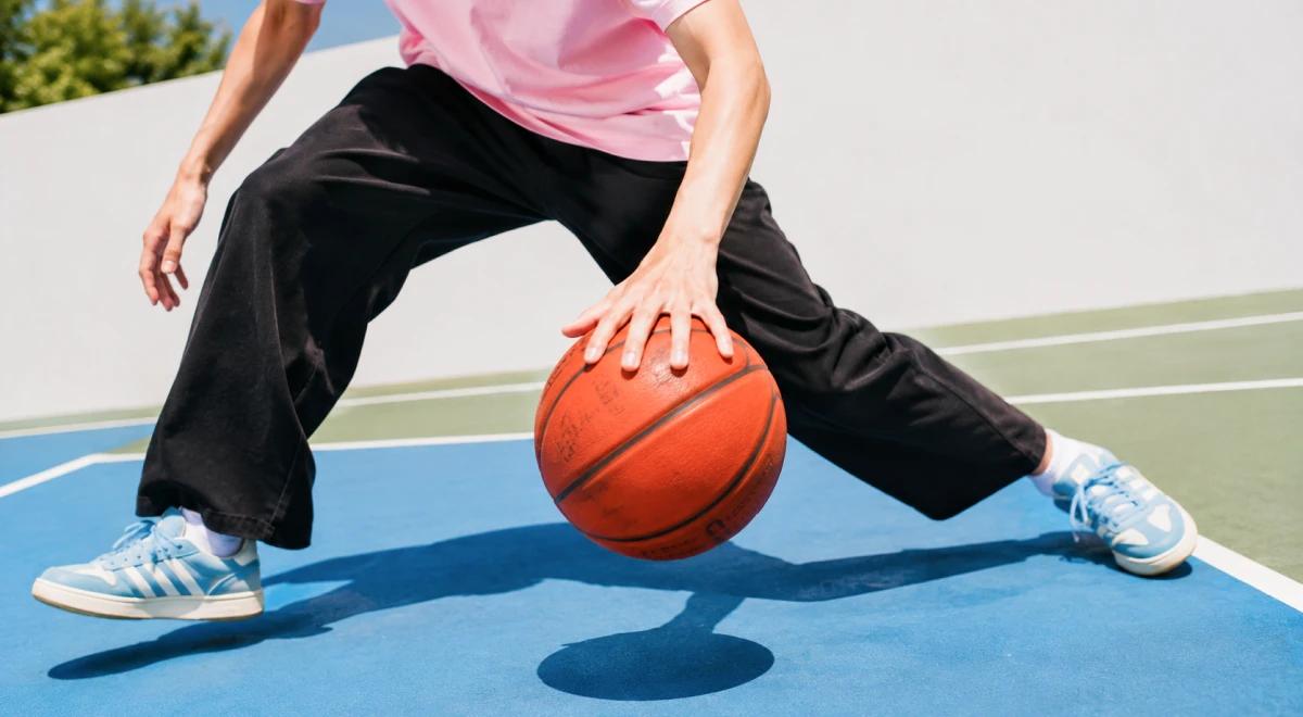 Young Asian man in a pink shirt dribbling a basketball on an outdoor court, representing physical activity and sports as a way to build self-esteem