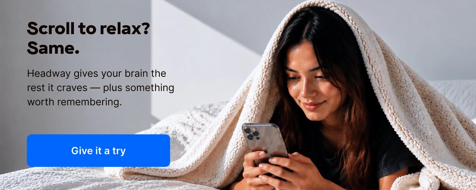 Smiling young woman relaxing in bed under a soft grey blanket while using a smartphone, representing mindful screen time with the Headway learning app