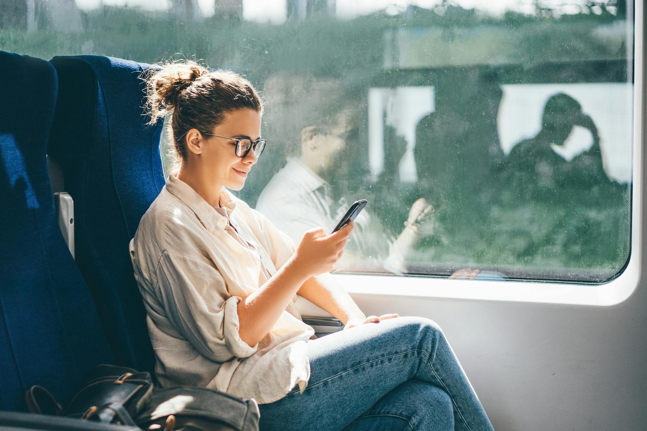A woman on the train wears glasses as she reads from her phone.