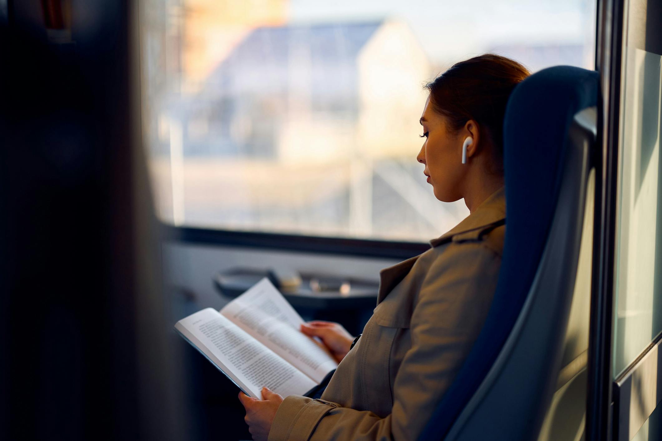 a woman sits on a train with an open book in her hands.