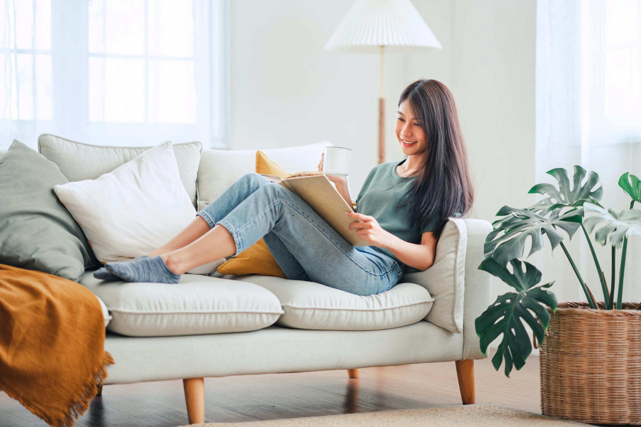A woman sits on a cream sofa reading a book.