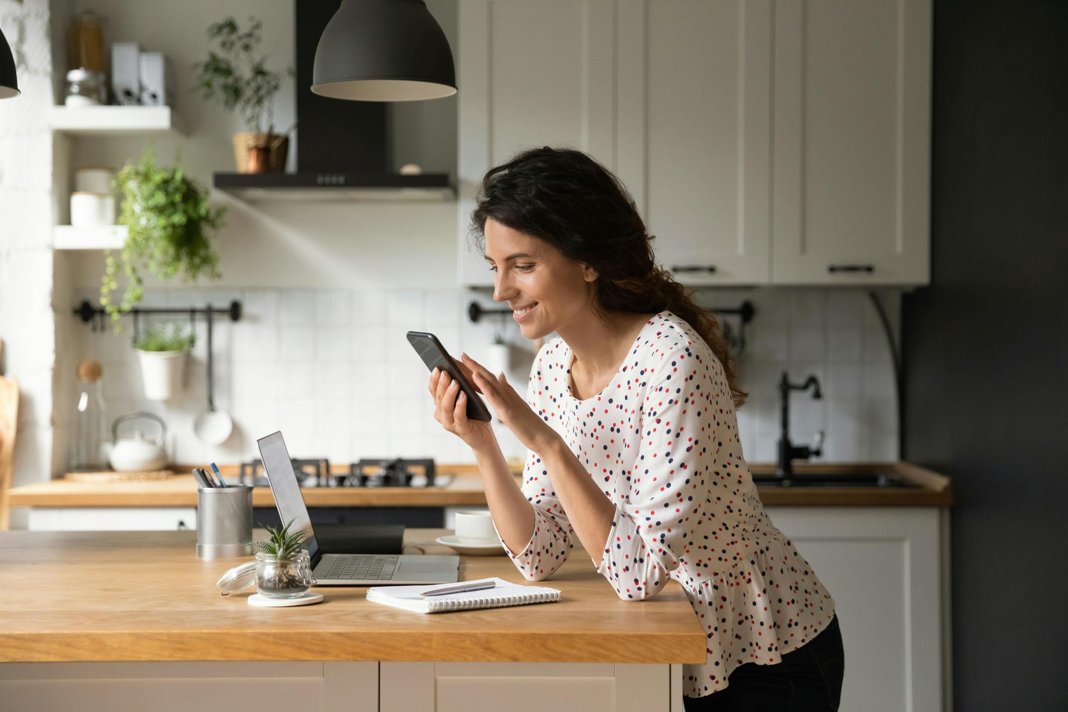 A woman stands in a kitchen reading from her phone.