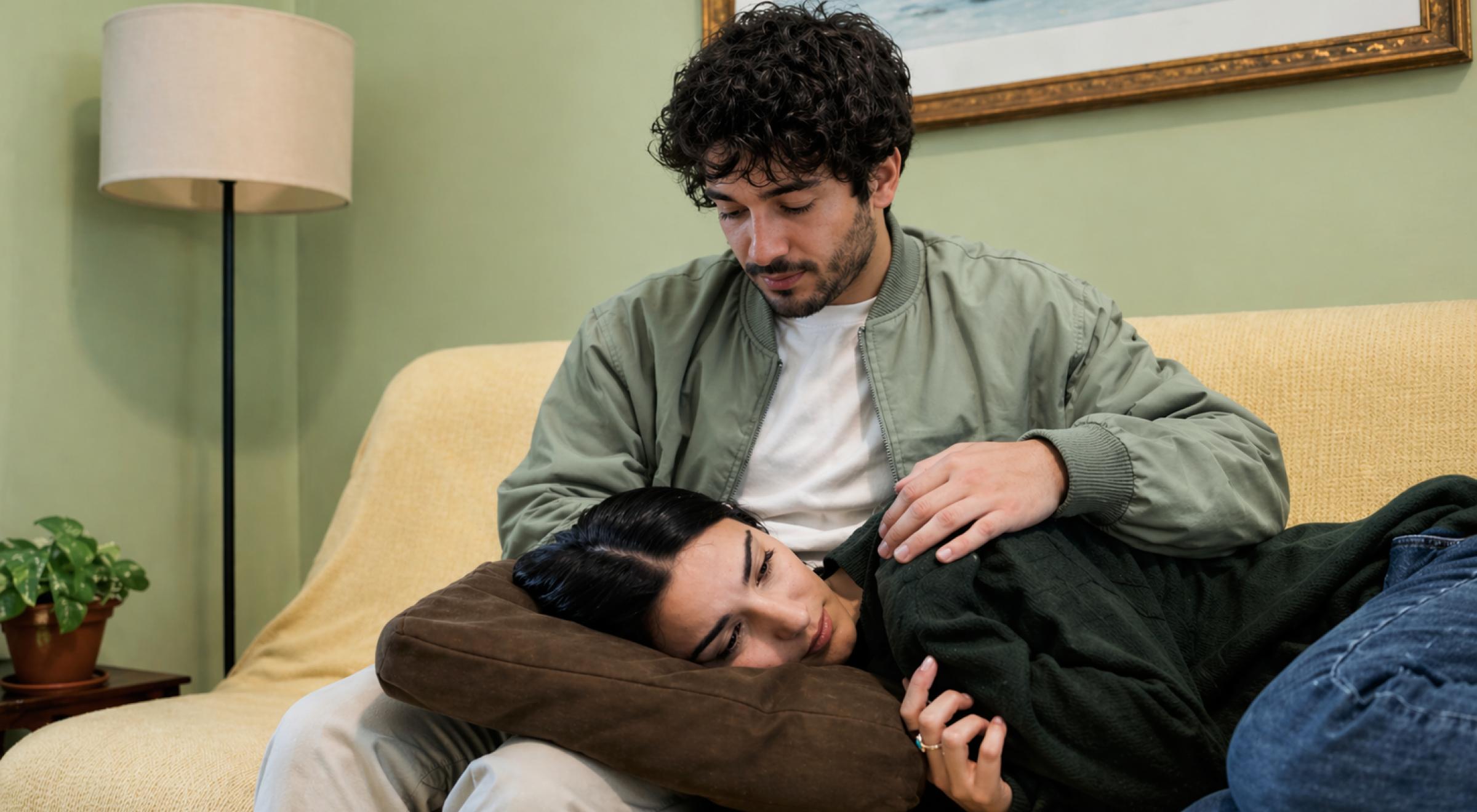 Man gently comforting a woman lying on a yellow couch in a cozy living room, illustrating emotional support dynamics in an anxious avoidant attachment style