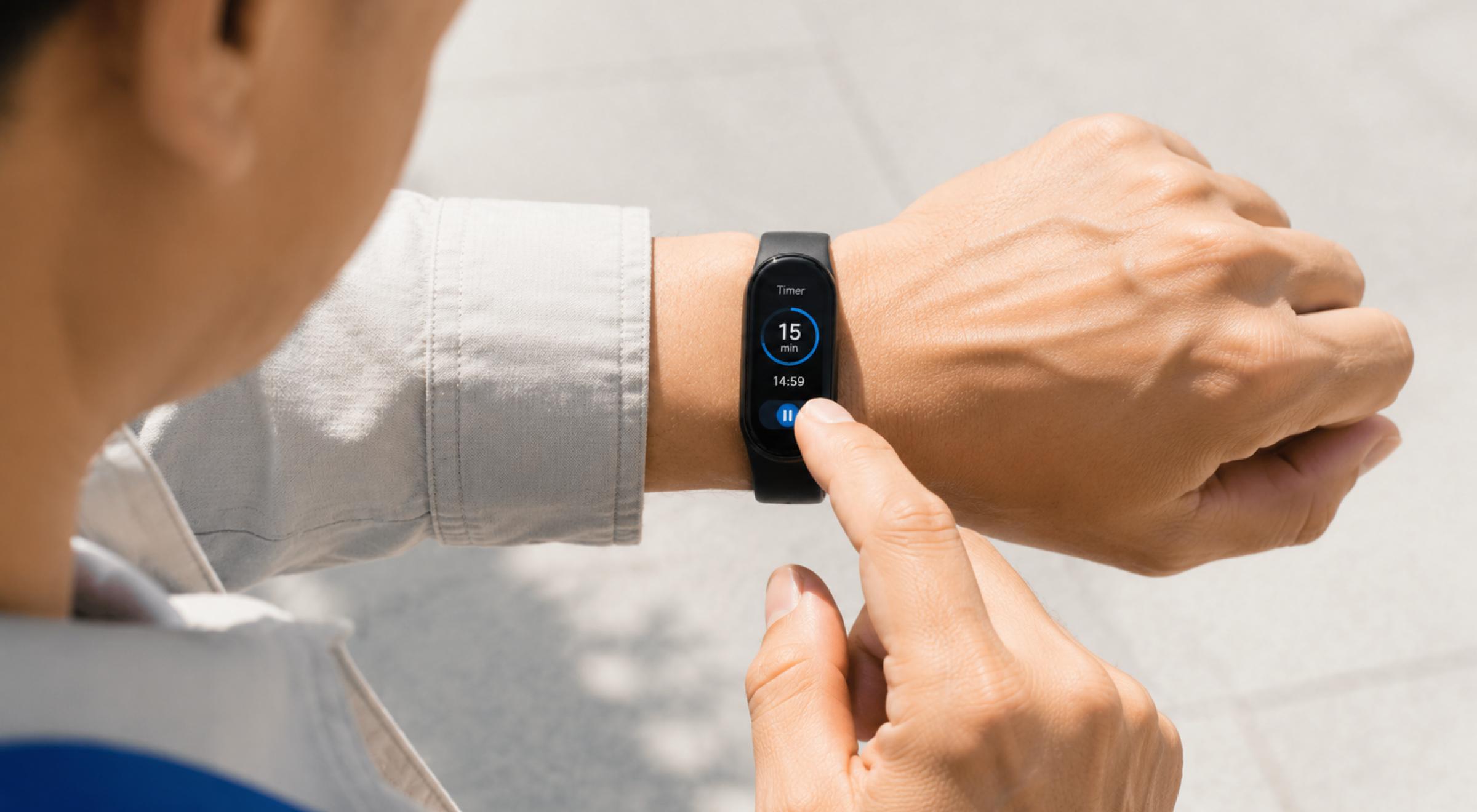 Person tapping a smart fitness band on their wrist outdoors, checking the display screen in daylight
