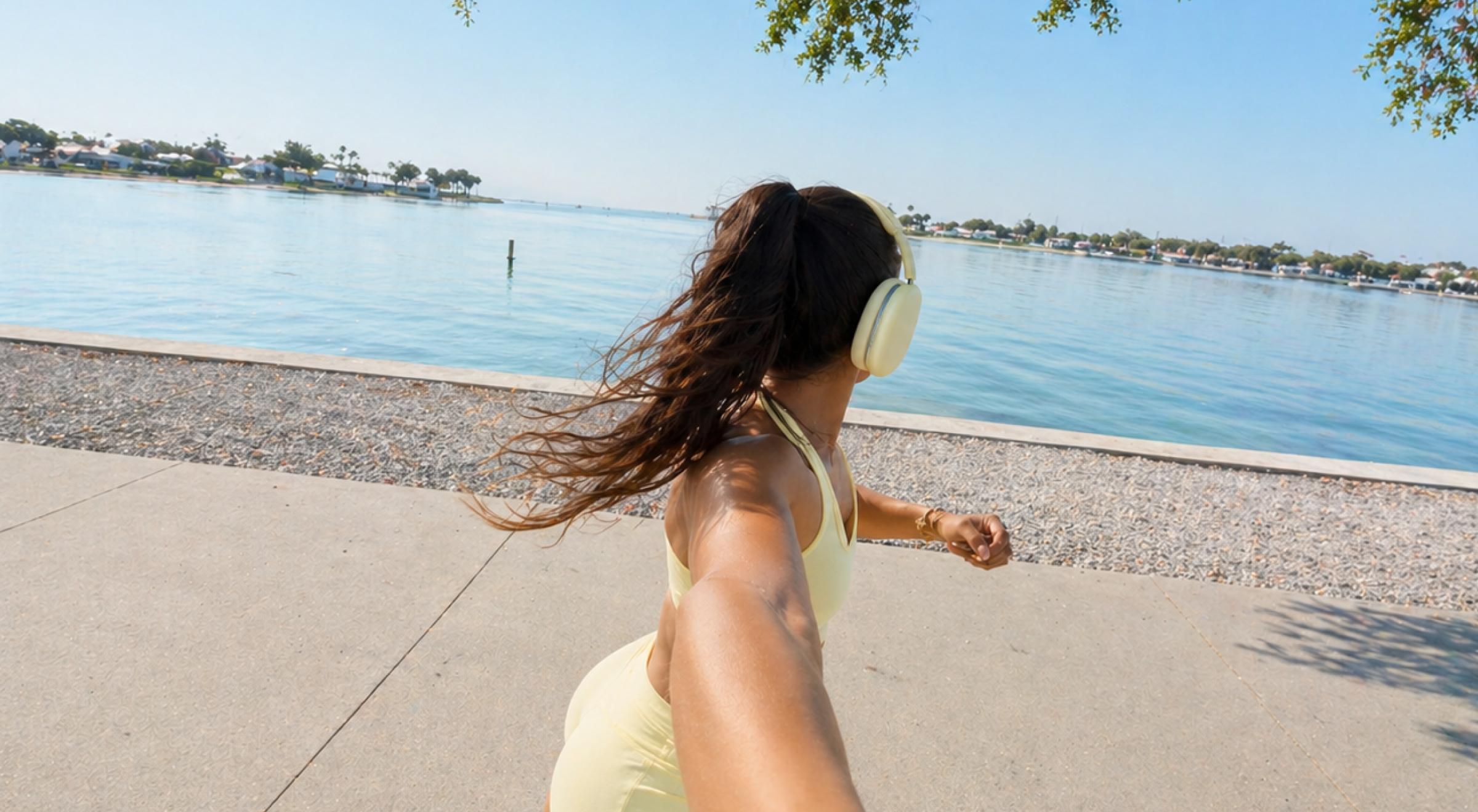 Woman in a yellow top and white headphones jogging along a sunny waterfront promenade as part of her glow up fitness routine