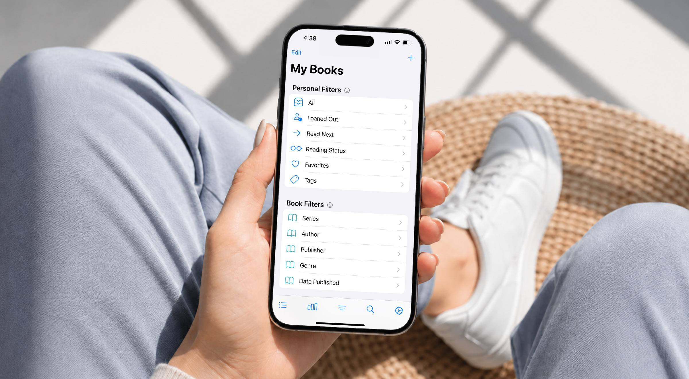 Person in light blue jeans holding a smartphone displaying the My Books screen with personal filters and book filters in the Buddy Book app, sitting in a wicker chair