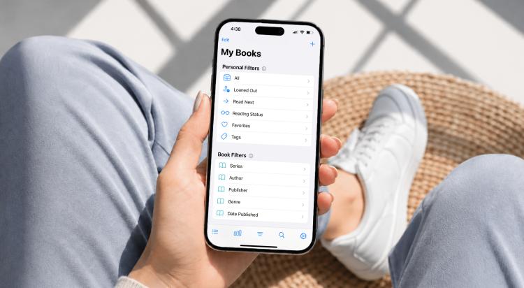 Person in light blue jeans holding a smartphone displaying the My Books screen with personal filters and book filters in the Buddy Book app, sitting in a wicker chair
