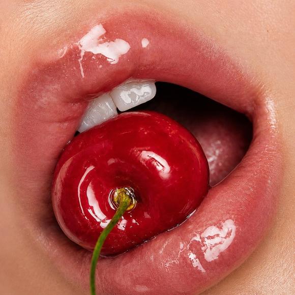 Close-up of glossy red lips holding a bright cherry between white teeth, evoking sweet self-care and personal growth themes