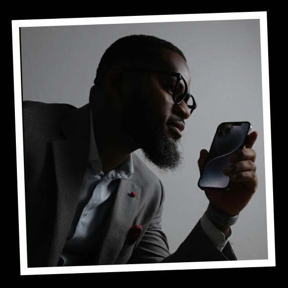 A blackskinned man in glasses holds and iphone in his hand