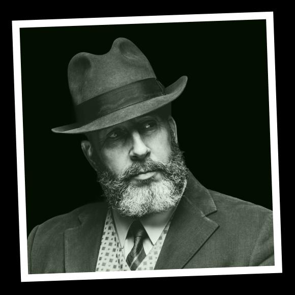 An old man with beard in hat and suit with a tie