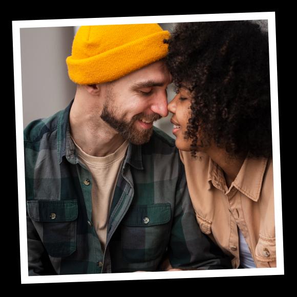 Man in yellow hat and black woman with curly hair are touching noses